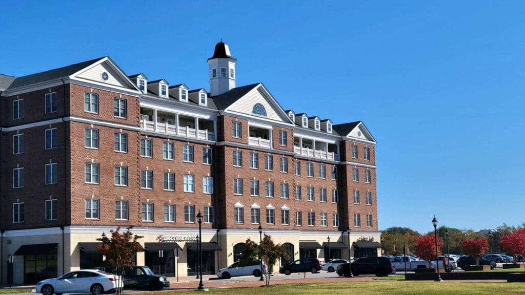 Brick multi-story apartment building with white trim and storefronts on the ground floor under a clear blue sky.