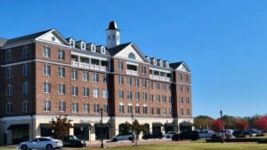 Brick multi-story apartment building with white trim and storefronts on the ground floor under a clear blue sky.