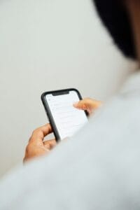Close-up of hands holding a smartphone displaying a list of search results on the screen, against a neutral background.