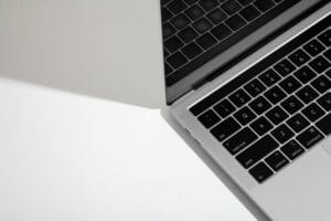 Close-up of a silver laptop keyboard, shown at a diagonal on a light surface, grayscale image.