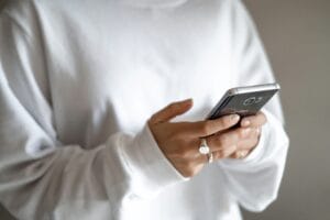 Person in a white sweater holds a Samsung smartphone with both hands, viewed from the side.