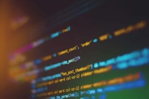 Blurred computer screen showing colorful lines of code with syntax highlighting in a dark setting.